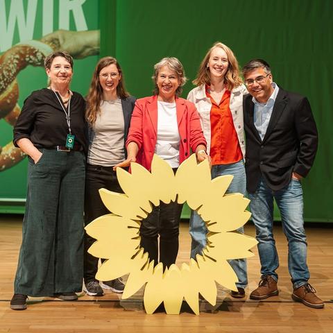 Foto von Theresa Eberlein, Steffi König, Gisela Sengl, Eva Lettenbauer und PAtrick Stenger. Sie stehen nebeneinander auf einer Bühne. Der Hintergrund ist grün. Vor ihnen steht ein großes gelbes Blumen-Podest.