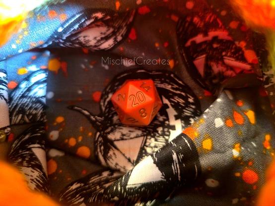 Inside the bag, which has a fabric lining with a Jack-o-lantern pattern. There's an orange d20 in the center.