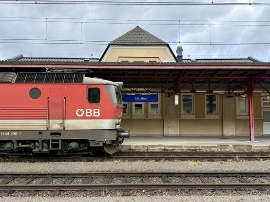 Blick auf Bahnsteig 1, an dem eine Lok steht. Dahinter von Dach hängt ein Stationsschild.