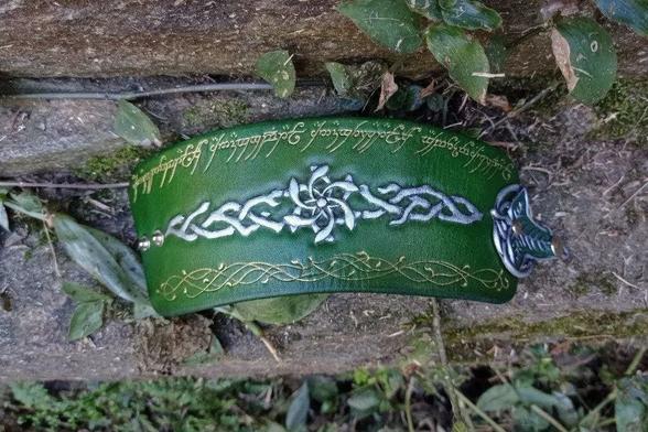 Green leather cuff with LoTR Galadriel's ring (Nenya) tooled on the front in silver, the Ring inscription along the top side and some vines tooled and the bottom and painted both in gold, and a Lorien leaf as the clasp, painted in silver and metallic green
