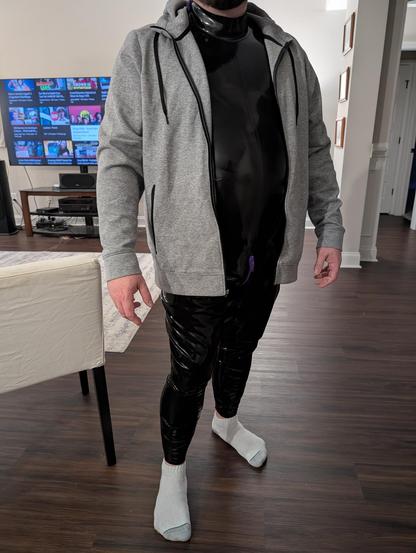 photo of me IRL with my black latex catsuit on, and a gray heather fabric zipper front hoodie on over it unzipped in front showing the black latex going neck to foot
