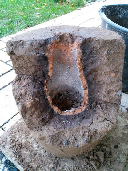 Der Ofen wurde für den Rücktransport wieder zerlegt. Man sieht hier in das Innere des Ofens: Ein ca. 8cm breiter Brennraum, der sich flaschenförmig nach oben verjüngt (Venturi-Effekt). Gut zu erkennen die etwa 1cm dicke rote Verziegelung der kompletten Innenwand, gefolgt von etwa 3cm dunkel gebranntem Lehm, und außen herum die lehmfarbene Hülle.