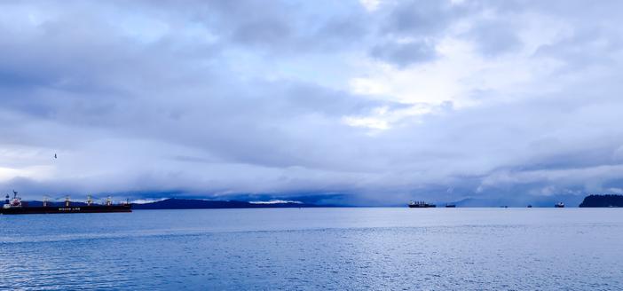 A wide color photo of ships in the Columbia River on a cloudy, stormy blue morning.
