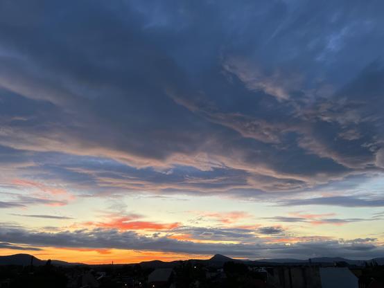 A vibrant sunset over distant mountains with a mix of orange, pink, and purple hues against a backdrop of dark and light clouds.