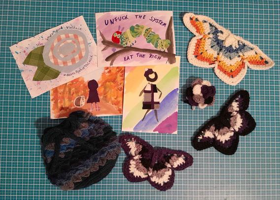 four mixed media postcards (watercolor + fabric scraps) and some crochet items: a dragonscale dice bag, an aroace butterfly, two ace moths and an ace rose. Everything is discribed in more detail in their own posts with #ACEAtelier2025