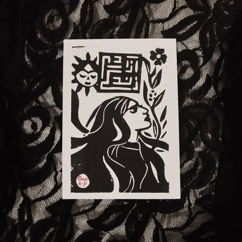 Linogravure imprimée  l'encre noire représentant une femme aux cheveux longs, de profil vers la droite de la feuille. Au fond, il y a un soleil Khorshid Khanom, ainsi qu'une plante avec une fleur. Il y a écrit Zan Zendegi Azadi (femme vie liberté) en calligraphie koufique.