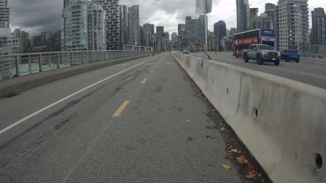 A photo from the middle of the Granville St Bridge, looking downtown. There's a more-or-less empty bike lane and sidewalk, a barrier, and a few cars on the road deck. There are some ominous dark clouds in the sky.