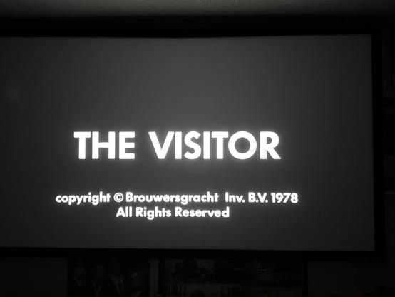 Shot of the words in all white black background 
“The visitor” on a film screen.