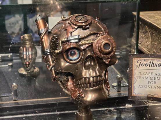 A photograph of a skull statuette that is heavily stylized with a steampunk theme, seen inside of a display case.