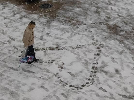 A woman walking in the snow to draw a heart