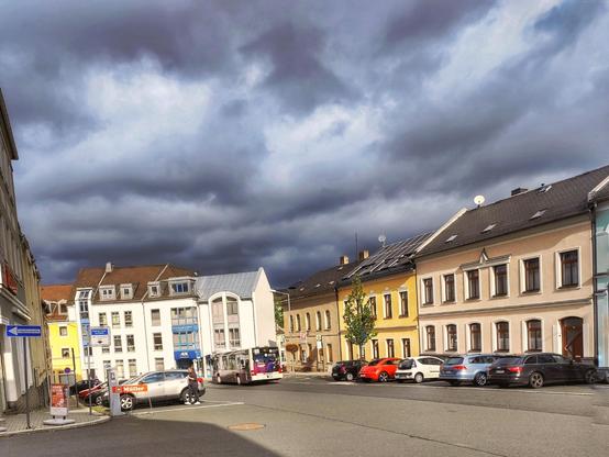 Eine Straße, die links, rechts und unten von Häuserzeilen begrenzt wird. Über allem dunkle, schwere Wolken.