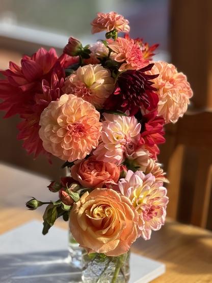 Bouquet of orange and red flowers in the sun. Flowers are dahlias and roses.