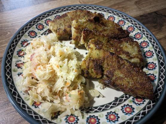 Na kolorowym talerzu leżą cztery dość grube plastry babki ziemniaczanej, a po ich lewej stronie porcja surówki z kiszonej kapusty.