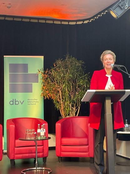 Eine Frau steht am Rednerpult und spricht ins Mikrofon.