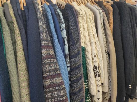 a rack of sweaters if all colours, lots of thick cream, blue and black