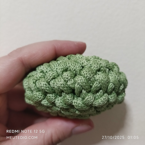 Lateral da peça de crochê verde, sendo segurada entre os dedos indicador e polegar de uma mão humana.