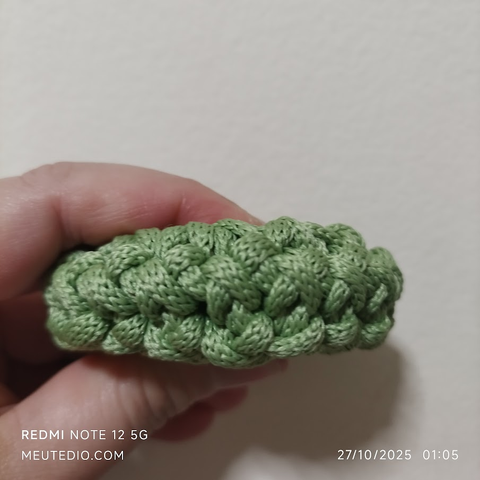 Lateral da peça de crochê verde sendo apertada por uma mão humana.