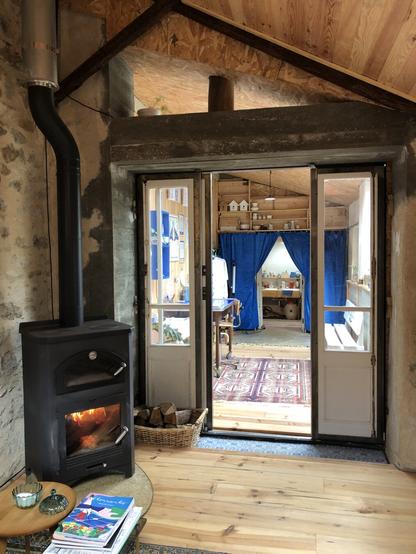 Contre champs de la salle tattoo. Vue sur le poêle à bois, qui me permet de chauffer l’espace lorsque les températures baisses. À travers la porte fenêtre, on aperçoit la salle bureau et en enfilade la salle remise-cuisine.