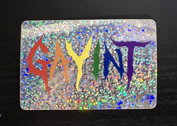 A sticker with a glitter background and the word "GAYINT" in stylized font and rainbow colors.