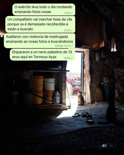 A imaxe mostra a entrada dunha vivenda moi humilde ou unha corte con paredes e o chan de pedra. Á dereita, hai varios bidóns e recipientes, e no chan, un par de sandalias. No centro, un gato está sentado na porta, mirando cara a fóra. A iluminación é escasa, con luz natural entrando pola porta aberta.

Sobre a foto hai unhas mensaxes de Whtasapp. A transcripción do texto das mensaxes:

12:01: "O exército leva todo o día rondando ensinando fotos nosas."
12:02: "Un compañeiro vai marchar hoxe da vila porque xa é demasiado recoñecible e están a buscalo."
12:02 (editado): "Asaltaron con violencia de madrugada ensinando as nosas fotos e buscándonos."
12:03: "Dispararon a un neno palestino de 13 anos aquí en Tormous Ayya."