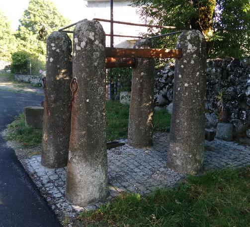 3 photographies numériques couleur de différents formats, qui représentent 3 modèles différents de travail à ferrer : tous comportent des montants dans lequel on bloque l'animal, dont on maiontient la patte le temps de poser un fer. 
Sur ce modèle, les montants sont de grands fûts en granits reliés par du bois et du fer, et on perçoit une chaîne et un cale-pied (patte) pour maintenir l'animal. Le sol est en pavés gris carré et le ferradou se situe en bordure d'un village.