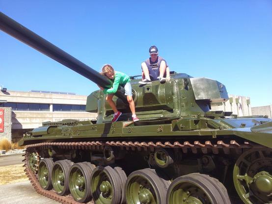 Classic Kiwi road trip break!

The photo was taken at the Waiouru Army Museum, with parts of the museum building visible in the background.

The kids are stretching their legs and having a climb on the big green tank outside the Waiouru Army Museum. The younger child, wearing a green top, is leaning on the long gun barrel near the front of the turret. The older child, wearing a blue cap, is sitting on top of the tank's turret, looking towards the camera. 

We swapped drivers and hit the halfway mark on our big drive from Wellington to Auckland for the summer holidays. The sun's out, and they're having a blast on the big gun, ready for the long haul up State Highway 1.

AltText created by Gemini Flash 2.5 with heavy revisions from a human.