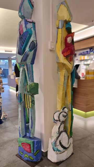 Dreimal aus verschiedenem Blickwinkel eine Gruppe von drei skulpturen aus bemalten Holz, gewesene Baumstämme, um eine betonsäule stehend gruppiert. Dargestellt sind menschenähnliche Figuren mit tierischen im Arm, affenähnliches an Bein geschmiert, Schlange um Leib gewunden... bunt und fantastisch.