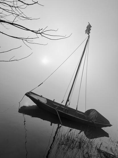 A typical Loire boat on the Loire River, parked near the bank in thick fog. (Version françæ) Bateau typique dal Loire sur læ Loire, garæ près dal berge par æn sacræ brouillard.