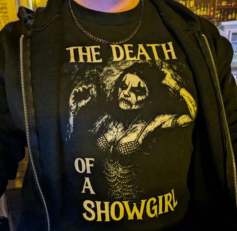 Photograph of a black T-shirt with a print that resembles Taylor Swift's latest album cover art, but has been heavily modified. The person in the artwork is wearing corpse paint.