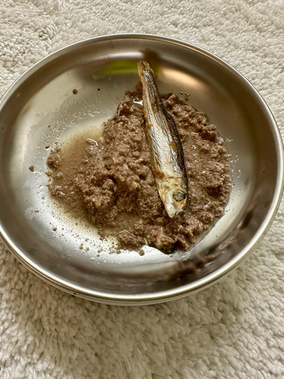 A freeze dried herring, some wet cat food inside a stainless steel bowl