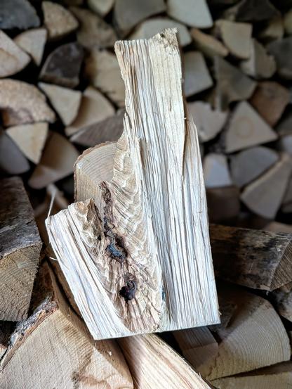 Detailaufnahme eines besonderen Holzscheits im Vordergrund eines Stapels, dessen Maserung und Form wie ein kleines Kunstwerk wirken. Foto by Johann Seidl, Gartenpoet.