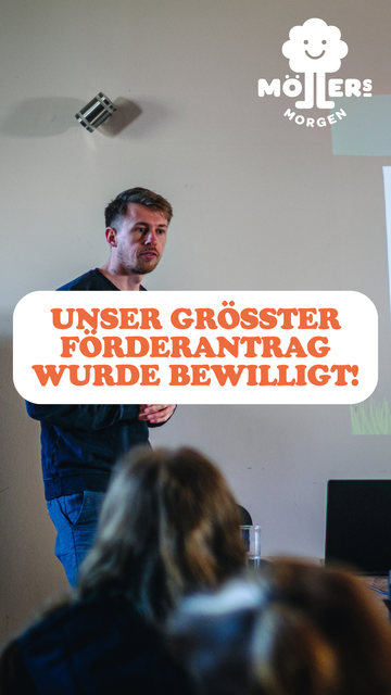 Das Bild zeigt einen Mann, der vor einer Gruppe von Menschen steht und einen Vortrag hält. Im Vordergrund steht in großen, orangefarbenen Buchstaben:
**"UNSER GRÖSSTER FÖRDERANTrag WURDE BEWILLIGT!"**
Das Logo von **Möllers Morgen** ist in der oberen rechten Ecke sichtbar. Die Szene wirkt wie eine wichtige Ankündigung oder ein Meilenstein für das Projekt oder die Organisation. Der Mann scheint engagiert und freudig die gute Nachricht mit den Anwesenden zu teilen.