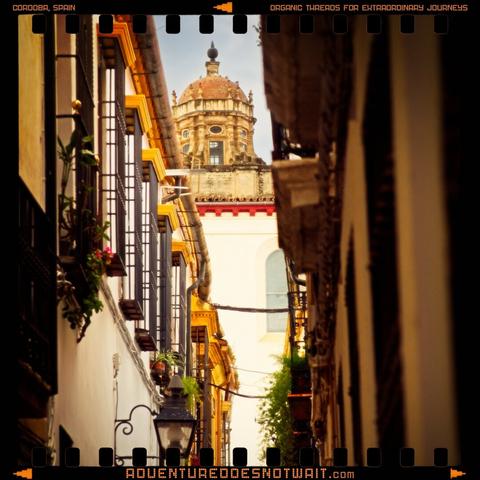 Narrow alleyway leading to a domed building in Córdoba, Spain, reflecting the organic threads and extraordinary journeys of our apparel