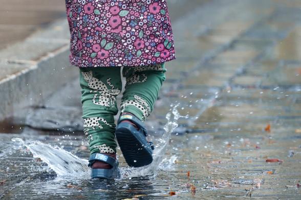 A kid shot from the back jumping in a puddle and splashing water