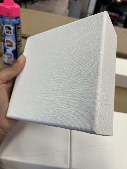 pic of my hand holding up a white, unpainted 6" x 6" canvas. it is very thick and sturdy, like holding a small fat book of some sort. there's two similar canvases on the table just below my hand, with a horizontal line drawn downwards across both of them in pencil.