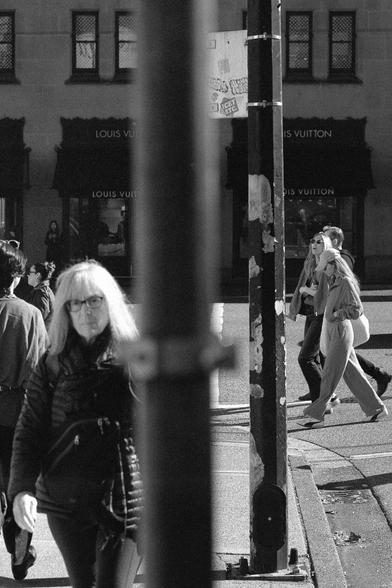 People move through an intersection filled with oblique light.