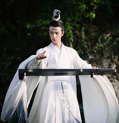Lan Wangji poised to unleash an attack with his darkly colored qin (also named) Wangji, left hand at the head of the qin and right hand at the ready to pluck a few inches above the strings toward the other end. His sleeves, and the qin's large tassel which fades in ombre from white to black, billow out to the sides and back. Lan Wangji keeps a careful eye on a target out of frame beyond the left edge of the image.