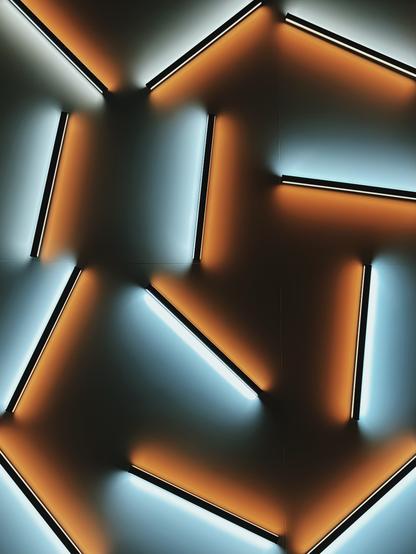 The image shows a three-dimensional, geometric letter "I" in an orange color. The letter is depicted in a modern, futuristic style with lighting and shadow effects that give it a plastic and three-dimensional appearance. The edges of the letter are highlighted with light lines, creating the impression that the letter is illuminated. The background is dark blue with subtle gradients transitioning to lighter shades, which further emphasizes the three-dimensional effect of the letter. The overall impression is abstract and technologically striking.