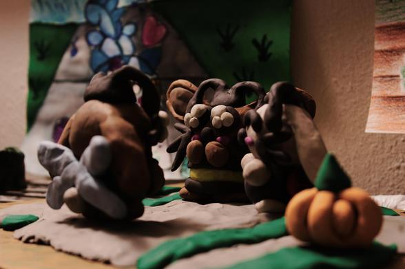 A modeling clay scene of a brown bunny dressed as a bee and a white lop bunny dressed as a ladybug posing while a brown lop bunny dressed as a dragonfly takes a photo of them posing.