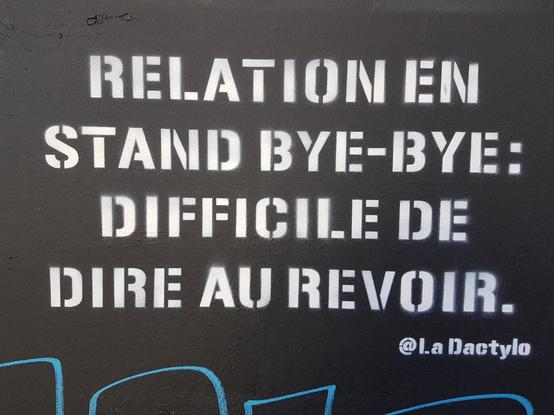 Graffiti "Relation en stand bye-bye; difficile de dire au revoir" écrit en lettres blanches sur mur fond noir. Signé @LaDactylo
