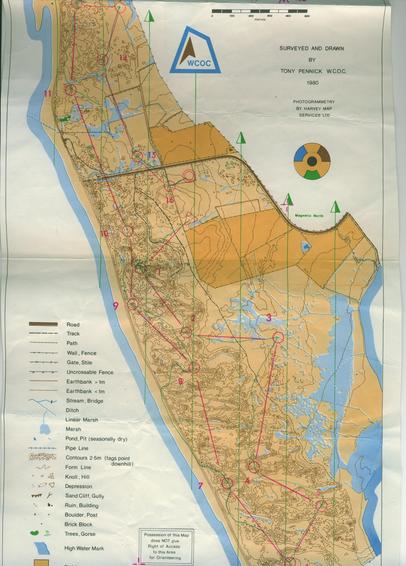 Four colour orienteering map of a sand dune area with the sea on the west and river on the east side.  Yellow screen used. There is a course marked, blue in modern standards.  The colour register roundel is in the form of a radiation warning symbol.