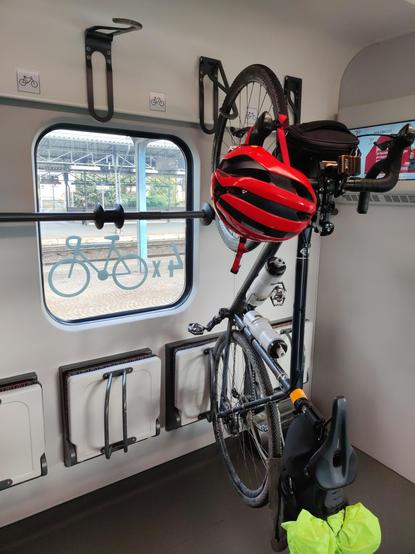 Na wieszaku w wagonie wisi rower z czerwonym kaskiem na kierownicy.
