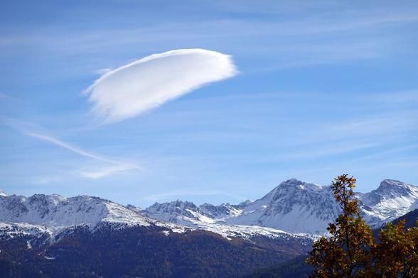 Blick auf verschneite Bergkette, schwarze Wälder, fast blauer Himmel, eine einzelne Föhnwolke,