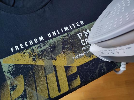 Ein Bügeleisen steht auf einem schwarz-gelben T-Shirt mit der Aufschrift "Freedom Unlimited".