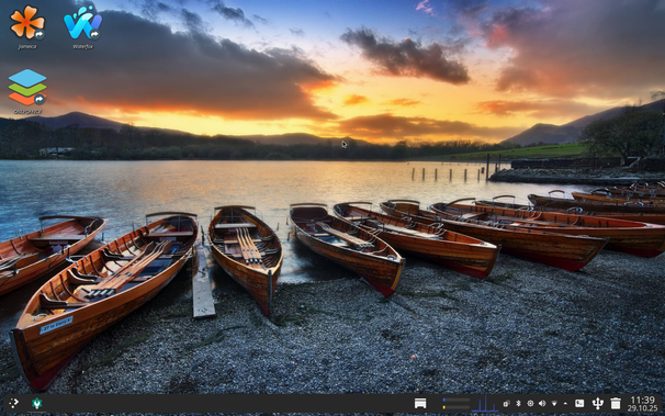 A computer desktop with icons for Jameica, Waterfox, and ONLYOFFICE in the top left, set against a wallpaper of wooden rowboats on a pebbled beach at sunset. The sky is dramatic with orange and blue hues. A taskbar is at the bottom, displaying the time "11:39 29.10.25".