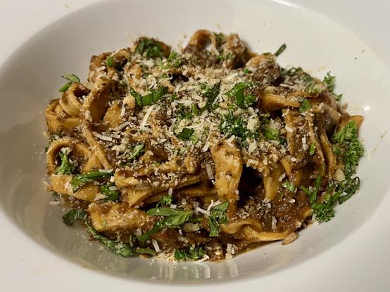A bowl of chunky pasta noodles dressed with a dark red-brown sauce and crumbs of bread, cheese and herbs