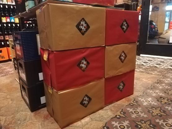 6 cartons empilés 3 par 3 et emballés de papier cadeau festif alternant les couleurs doré et rouge avec un autocollant Biérocratie blanc sur fond noir sur le devant.