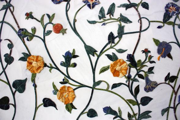 A closeup of the tile vine motif on the white walls. Te fine and leaves are a dark green and the flowers are a variegated yellow/orange. Some buds are an orange-red.