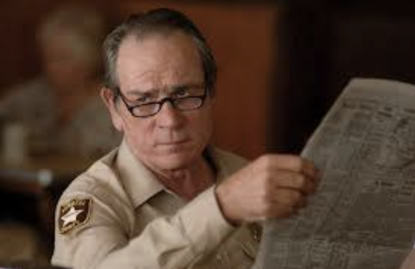 Screengrab: Tommy Lee Jones from "No Country for Old Men" looking over his reading glasses, newspaper in hand.
