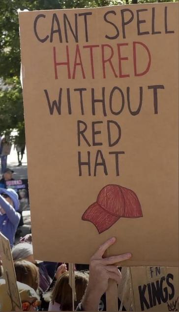Sign that says “YOU CAN’T SPELL HATRED WITHOUT RED HAT” and a drawing of a red baseball cap.
